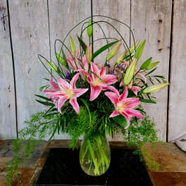 Pink lilies arranged in a clear glass vase with trailing greenery