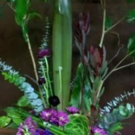 Tall tropical floral arrangement with purple blooms in a white container