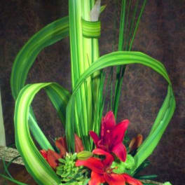 Modern floral arrangement with red lilies and green looped leaves in a blue bowl