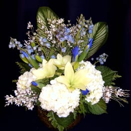 White hydrangeas and pale yellow lilies in a basket with blue accents