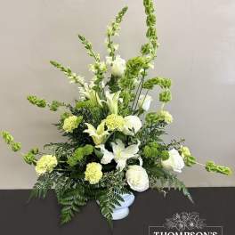 Tall white and green arrangement with lilies, roses, carnations, and Bells of Ireland in a white vase