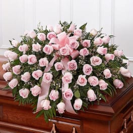 Pink rose casket spray with ribbon on a wooden coffin