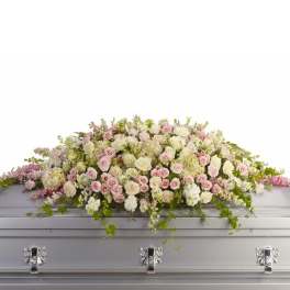 Pastel pink and white rose casket spray draped across a silver casket.