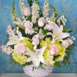 Basket arrangement of white lilies, pink roses, and pale hydrangeas