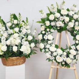 White floral wreath on an easel beside a white flower basket arrangement