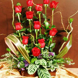 Tall arrangement of red roses with decorative foliage in a low container