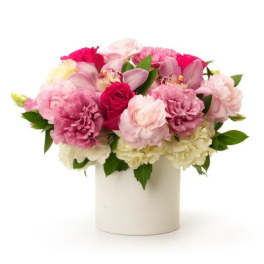 Low pink and white arrangement with roses, carnations, and orchids in a white cylinder vase