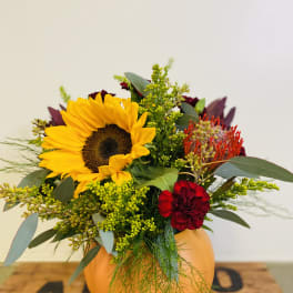Sunflower and red floral arrangement in an orange pumpkin vase