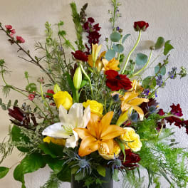 Tall mixed bouquet with lilies, roses, and red blooms in a black vase