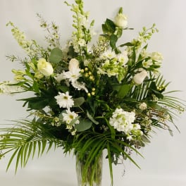 White floral arrangement in a clear glass vase with tall greenery