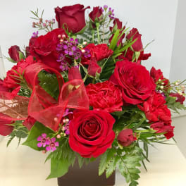 Red roses and carnations in a square vase with a red ribbon
