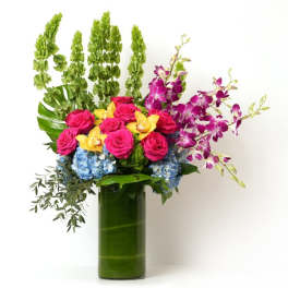 Tall arrangement of pink roses, orchids, and blue hydrangeas in a green-lined glass cylinder vase