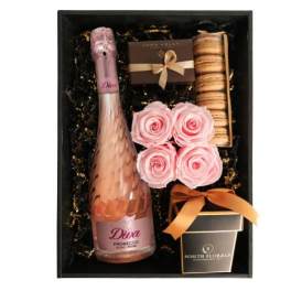 Gift box with pink sparkling wine, pink roses, macarons, and chocolates