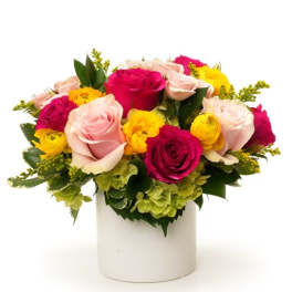 Low arrangement of pink and hot pink roses with yellow blooms and green hydrangea in a white cylinder vase
