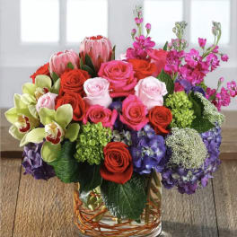 Mixed bouquet of roses, orchids, hydrangeas, and protea in a glass vase