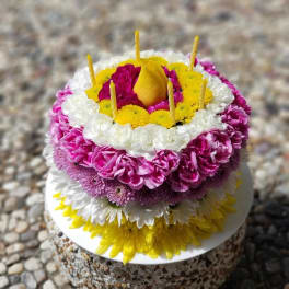 Round floral cake with pink, white, and yellow flowers and candles