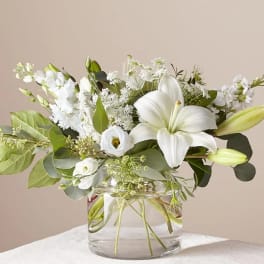 White lilies and mixed white flowers in a clear glass vase