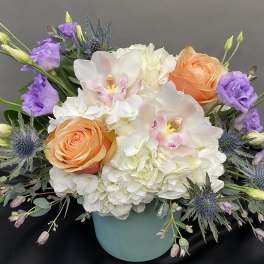 Bouquet of white hydrangeas, peach roses, and purple flowers in a blue vase