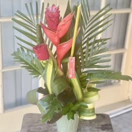 Tropical arrangement with red heliconia and palm leaves in a mint vase