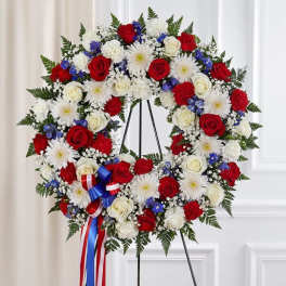 Standing wreath of red and white roses and mums with blue accents and a patriotic ribbon bow.