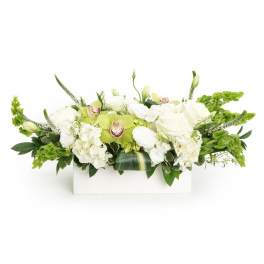 Low white and green floral centerpiece with roses, hydrangeas, and green orchids in a white rectangular container