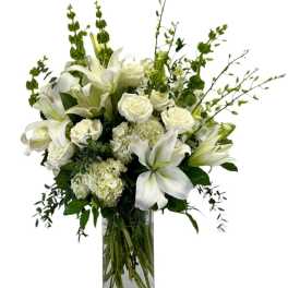 Tall arrangement of white lilies, roses, hydrangeas, and bells of Ireland in a clear glass vase