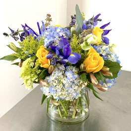 Bouquet of yellow roses, blue hydrangeas, and purple flowers in a glass vase