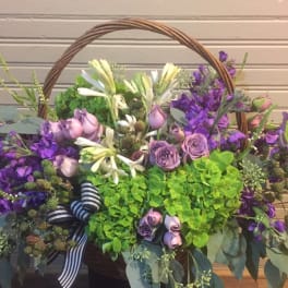 Basket arrangement of purple and white flowers with a striped ribbon