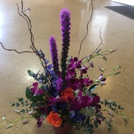 Tall floral arrangement with orange roses and purple orchids in a vase