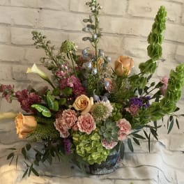 Mixed bouquet with peach roses, pink blooms, and tall green spikes in a vase