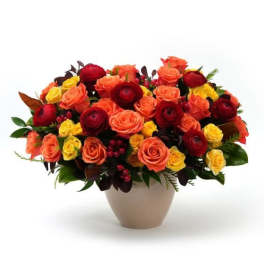 Low vase arrangement of orange, red, and yellow roses with dark red blooms