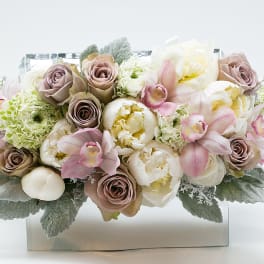 Pastel bouquet of roses, peonies, and orchids in a clear rectangular vase