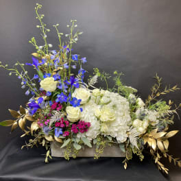 Mixed floral arrangement with white roses, blue flowers, and gold foliage in a low container