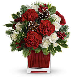 Red and white floral arrangement in a clear square vase with pinecones