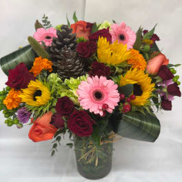 Mixed bouquet with roses, gerbera daisies, sunflowers, and pinecones in a glass vase