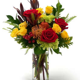 Tall arrangement of red and yellow roses with green hydrangea in a clear glass vase