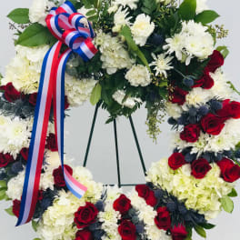 Floral wreath with red and white flowers and a tricolor ribbon on a stand