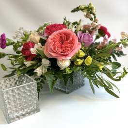 Mixed bouquet in a square glass vase with pink, red, purple, and yellow flowers