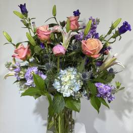 Mixed bouquet of pink roses, lilies, and purple flowers in a glass vase
