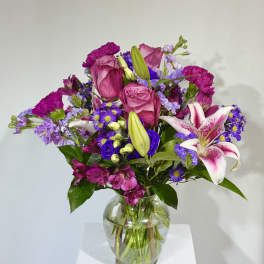 Bouquet of pink roses, lilies, and purple flowers in a glass vase