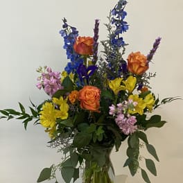 Mixed bouquet of orange roses, blue delphinium, and yellow alstroemeria in a glass vase