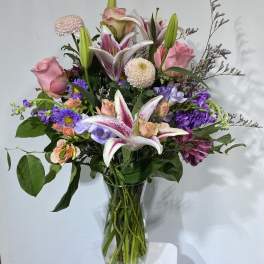 Mixed bouquet of pink roses, lilies, and purple flowers in a glass vase