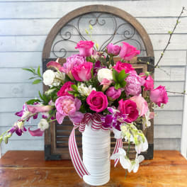 Pink and white floral arrangement in a white vase with striped ribbon