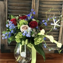 Bouquet of red and blush roses with blue flowers in a glass vase