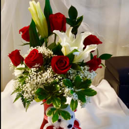 Red roses and white lilies in a red vase with a teddy bear