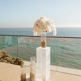 White orchid arrangement on a tall clear pedestal by the ocean