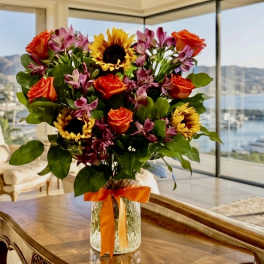 Bouquet of sunflowers, orange roses, and pink flowers in a glass vase