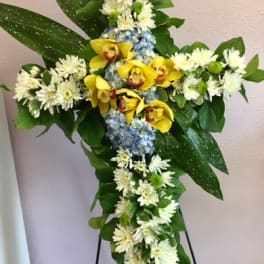 Cross-shaped floral arrangement with yellow orchids, white daisies, and blue hydrangea
