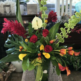 Tropical bouquet with red roses, yellow calla lilies, and green orchids in a glass vase