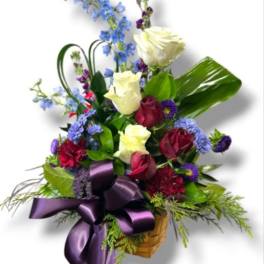 Basket arrangement of roses, blue flowers, and a purple ribbon